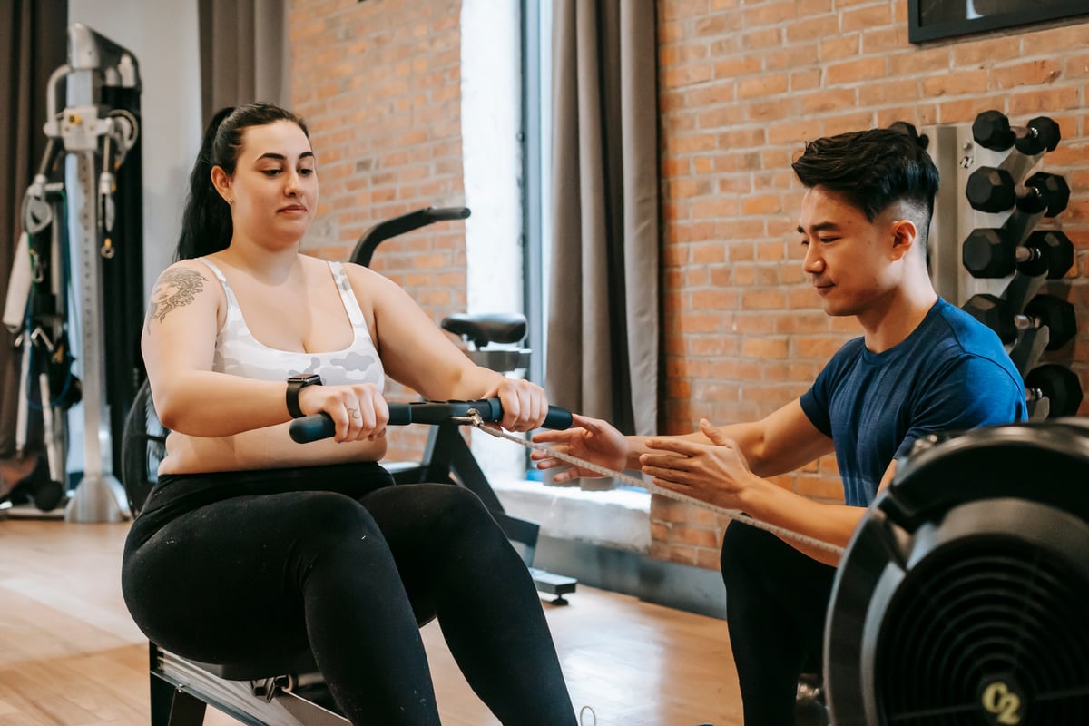 Focused young male trainer helping woman to do pulling exercise